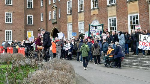 A group of people gathered outside a building, holding placards and protesting.