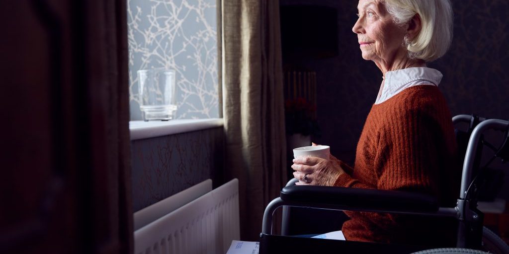 Senior Woman In Wheelchair With Energy Bill By Radiator In Cost Of Living Energy Crisis